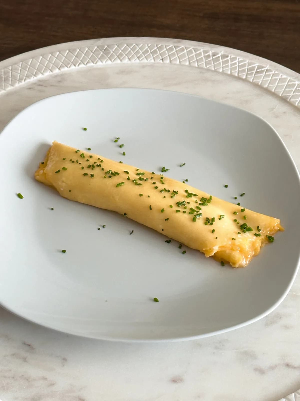 A pale yellow french omelette folded onto a plate with chives