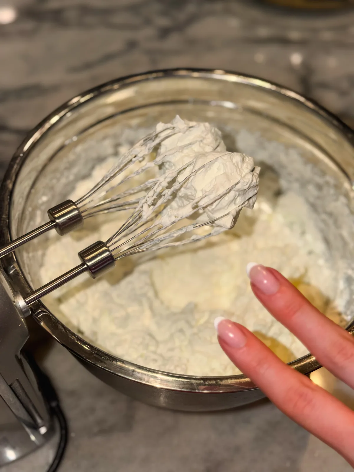 Hands holding a whisk full of pale whipped cream, throwing a peace sign
