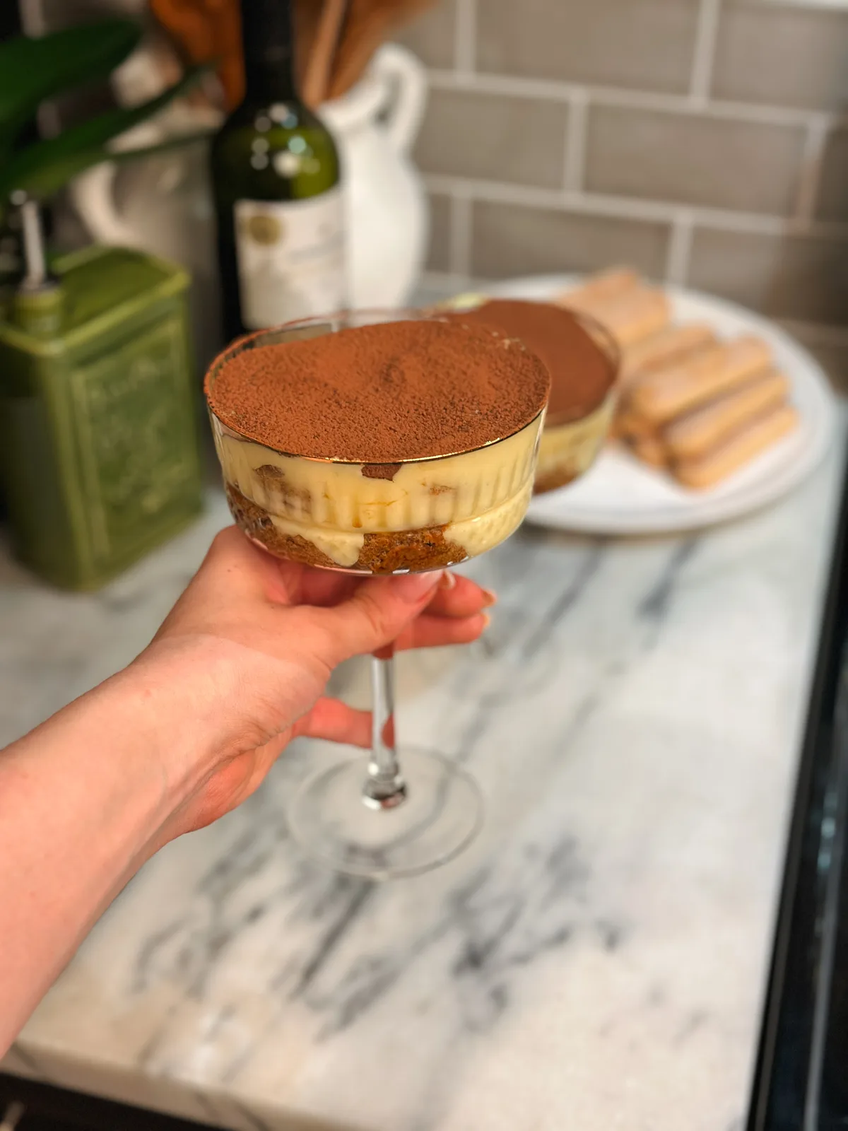 A piece of tiramisu held in hand, dusted with cocoa