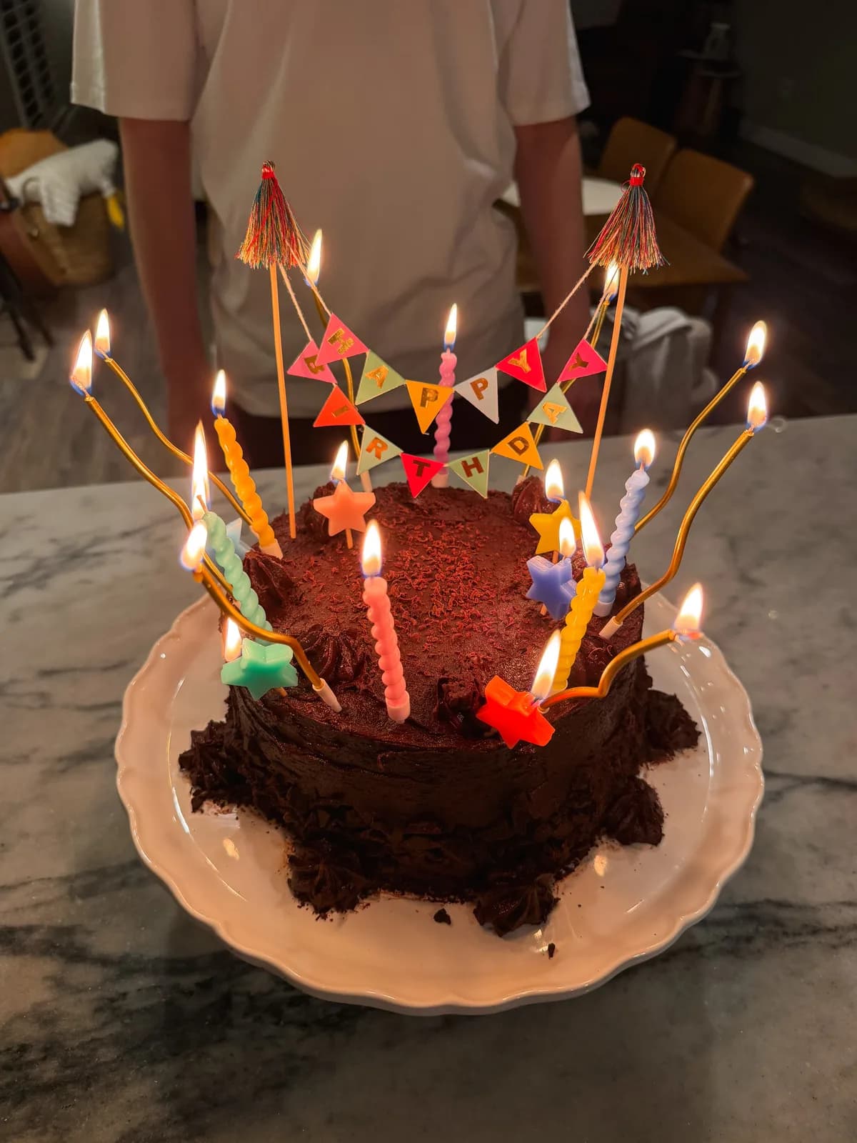 A tall chocolate layer cake with thick fudge frosting on a vintage stand